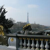 An iron-and-gold metalwork that looks like a man, on a bridge with the Eiffel Tower in the distance 