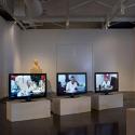 a gallery exhibit with three TVs displaying people 