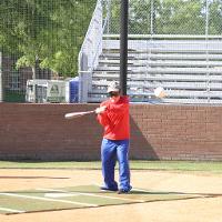 A blindfolded camper swings a baseball bat at an oncoming baseball.