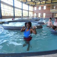 A small group of campers swims in the lazy river in the CSU rec center. One poses for the camera, holding two thumbs up.