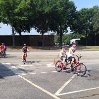 A group of campers rides on bikes around a large parking lot.