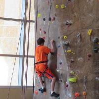 A camper wearing all orange climbs up the rock wall in the CSU rec center.