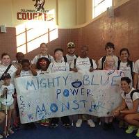 A group of campers poses for the camera. The campers in the front of the group hold up a large sheet of white paper with the phrase "Mighty Blue Power Monsters" written across it in blue marker and has the campers' names written on it.