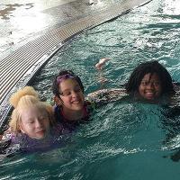 Three campers swimming in the pool at the CSU rec center pose together for the camera.