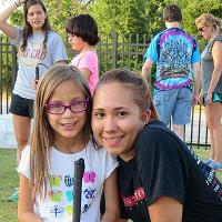 A camper and a camp counselor pose for the camera in front of a few counselors and campers in the background.