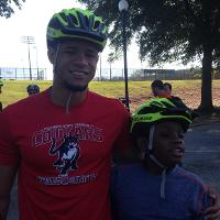 A camper and a camp counselor wearing bike helmets stand together and smile for the camera.