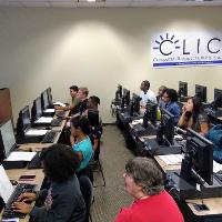 a computer lab with a number of students working on computers with an assistant watching
