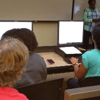 two students on computers with someone else watching
