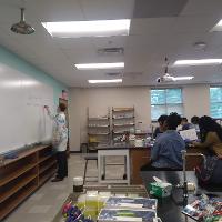 several students and adults sitting in a classroom watching a teacher write on the board