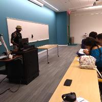 several students and adults sitting in a classroom while a male teacher talks at the front