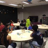 several students and adults sitting in a classroom listening to a student talk at the front
