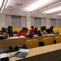 several students and adults sitting in a classroom with a number of yellow chairs