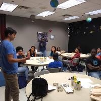 several students and adults sitting in a classroom listening to a student talk