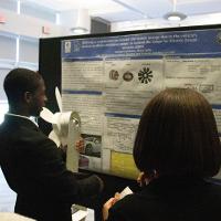 a male student discussing a presentation display to several people watching