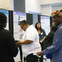 multiple people viewing a presentation display while a female student talks in the background