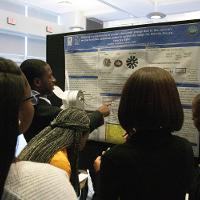 a male student discussing a presentation display to several people that are watching