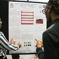 a female student discussing a presentation display to another person while pointing at the presentation
