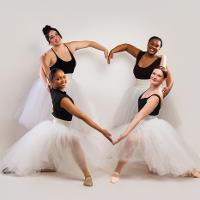 Four female ballet students in a circle connecting arms in the shape of a heart