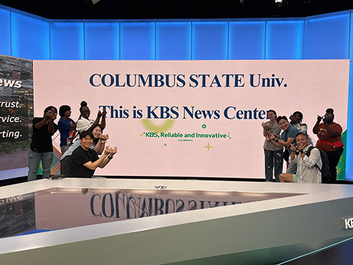 several people sitting and standing around a news anchor desk