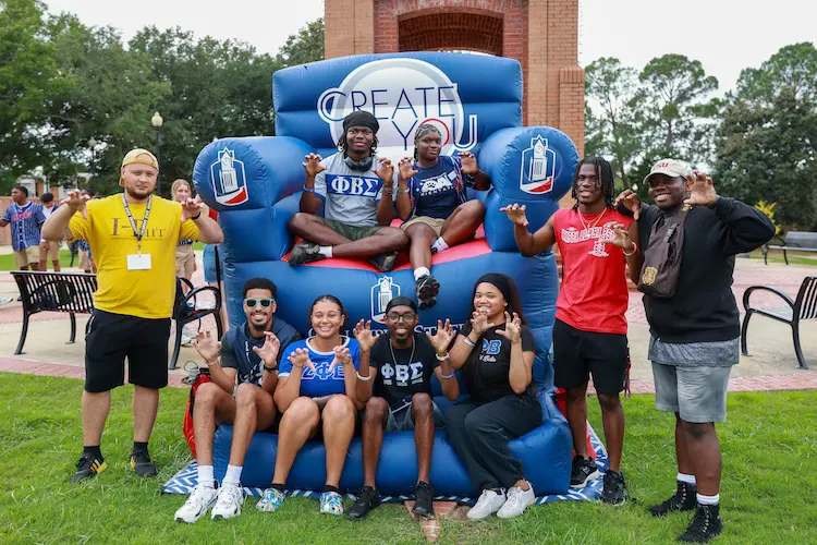 Sorority and fraternity members posing on a large blow up chair outside the clock tower
