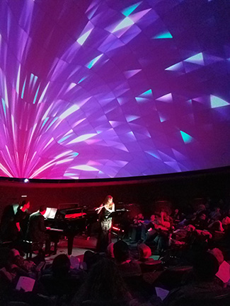 Katie Woody performing a flute solo in a theater with lighting effects