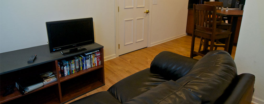 common area with a black leather couch, TV on a media console, table, and chairs