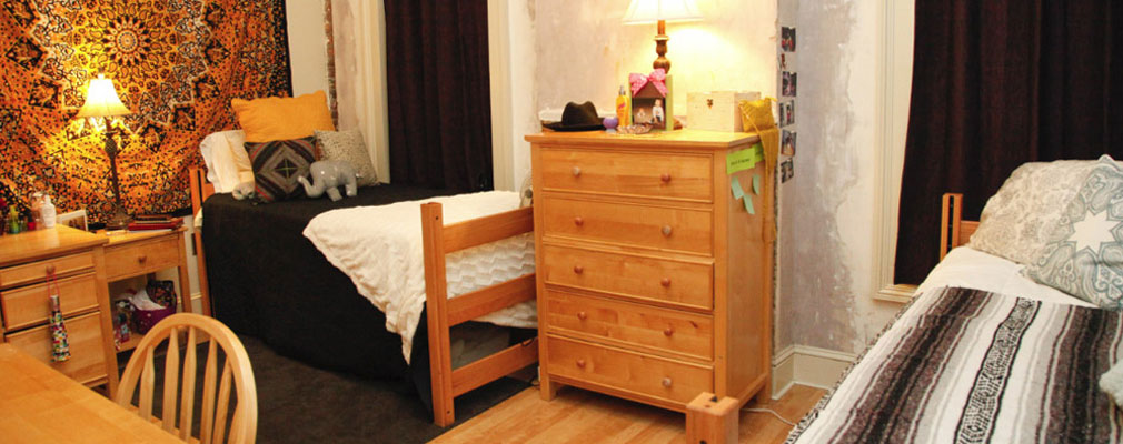 a bedroom with two loft beds, a dresser, a nightstand, a desk, and two large windows covered by curtains