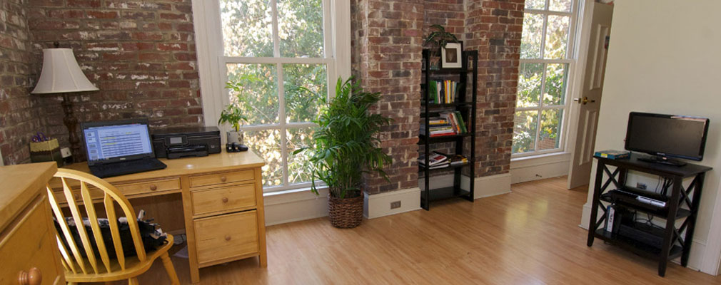 common area with a desk, TV stand on a media console, a faux plant, a bookshelf, and two large windows