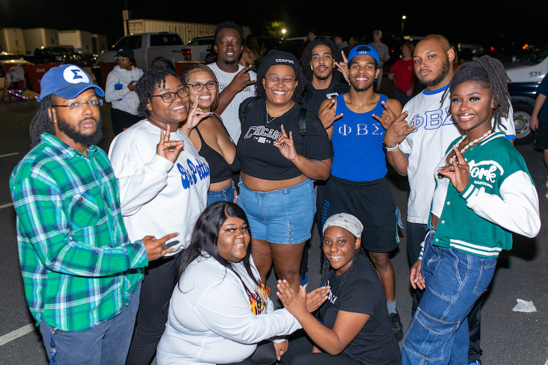 Sorority and fraternity members posing outside, smiling, some making hand symbols