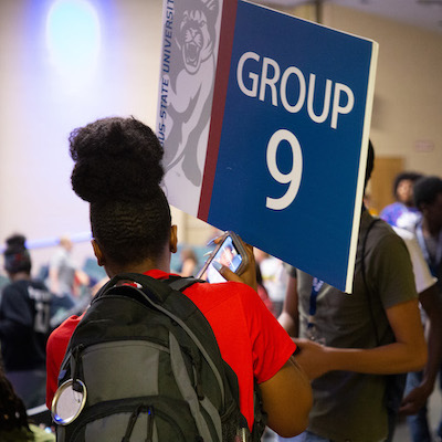 person holding an orientation sign and students walking in group