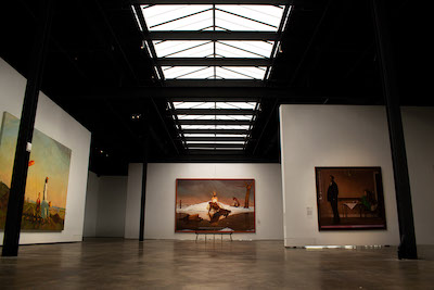 Large paintings hanging in a gallery with a skylight in the ceiling