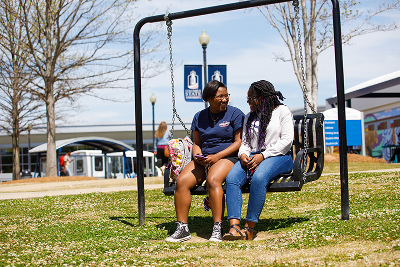 two female students sitting on a swing talking to each other