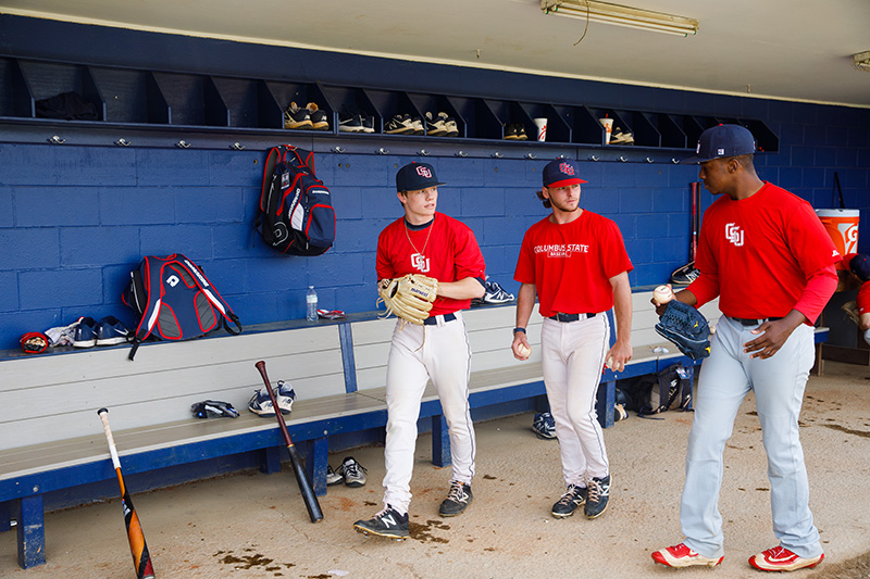 three male students in baseball uniforms walking and talking with each other